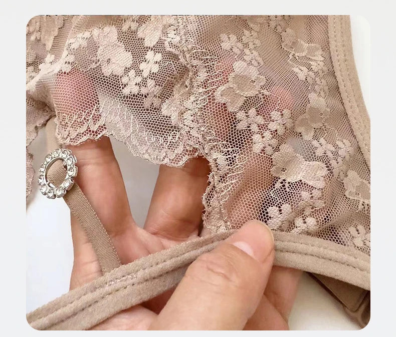 Close-up of a beige lace bra with floral lace detailing and a hand holding the underband to show the stretch and strap attachment.