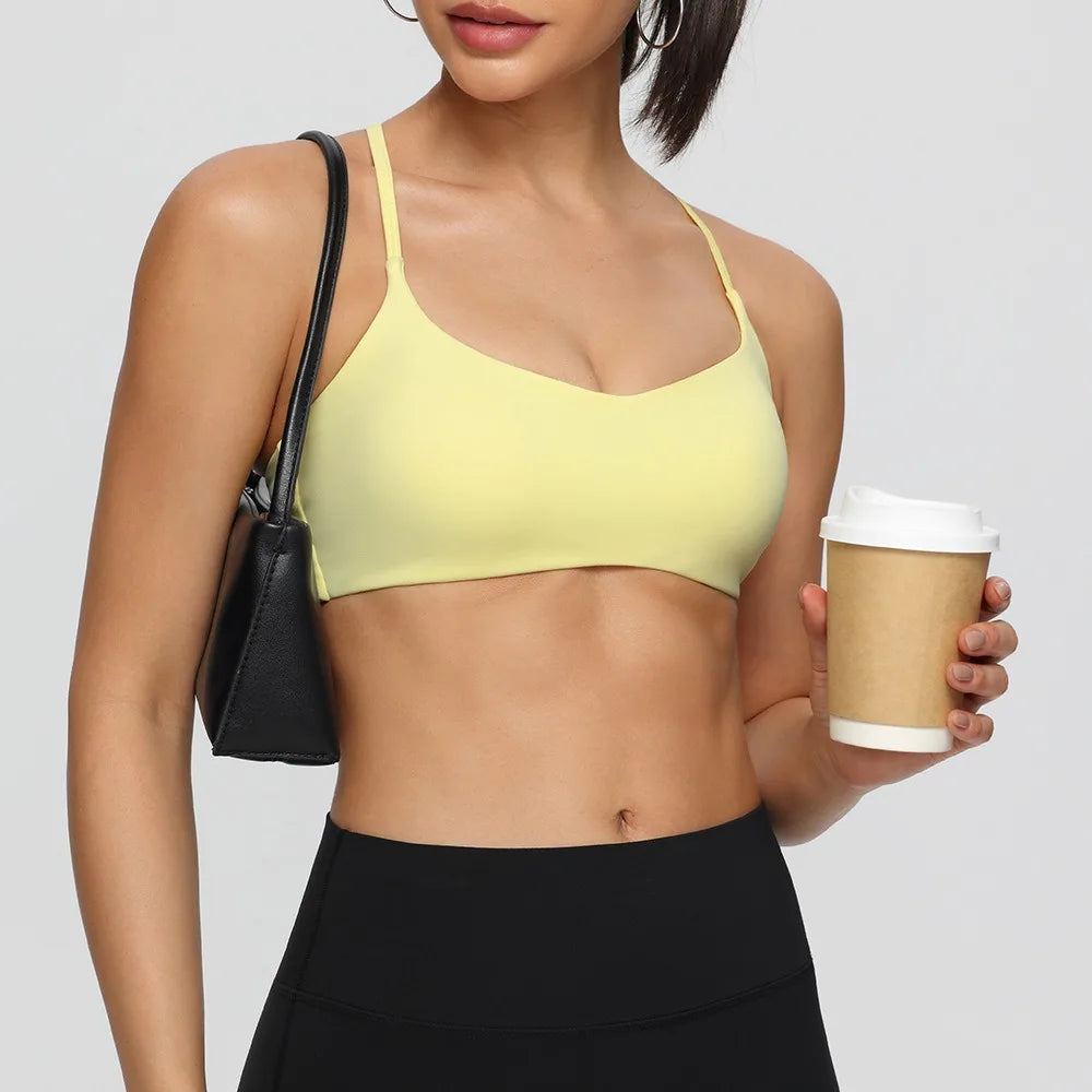 Woman wearing a yellow sports bra and black leggings, holding a coffee cup.