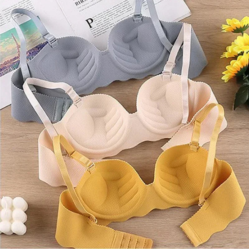 Three bras in gray, beige, and yellow on a wooden surface with flowers and a magazine.