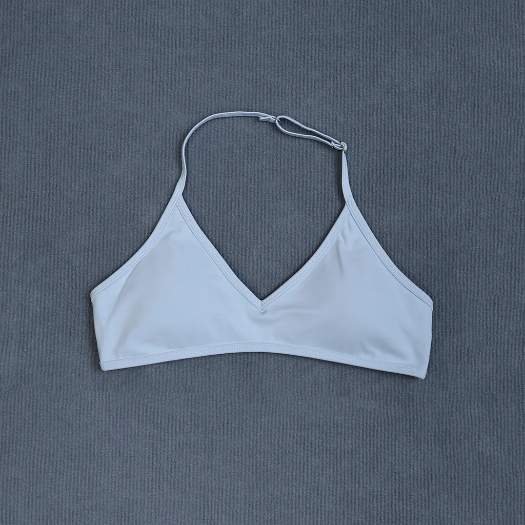 A light blue V-neck bikini top with thin adjustable shoulder straps and a back strap closure, laid flat on a textured gray background.