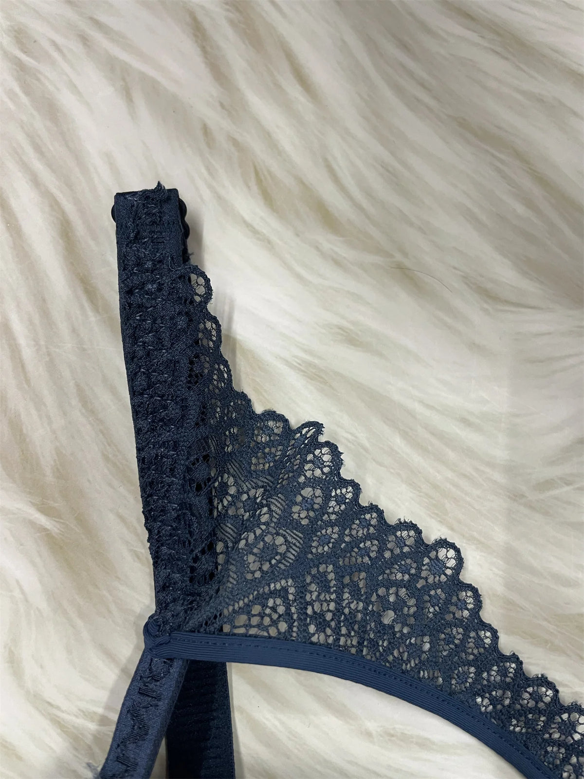 A close-up of a navy blue lace thong or lingerie piece laid flat on a white faux fur background.
