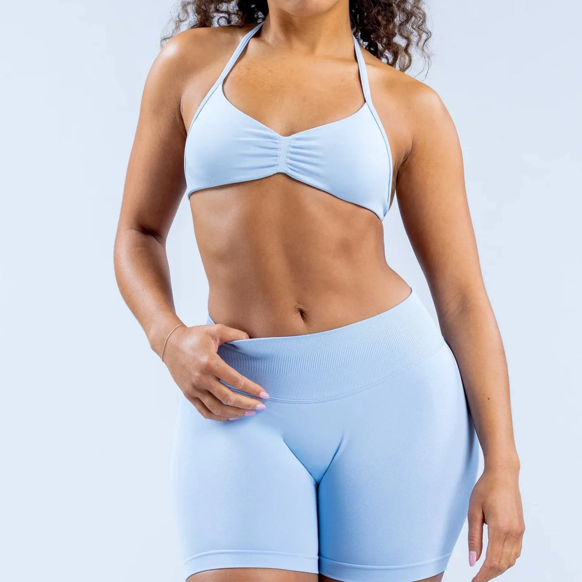 Person wearing a light blue sports bra and shorts set on a plain background