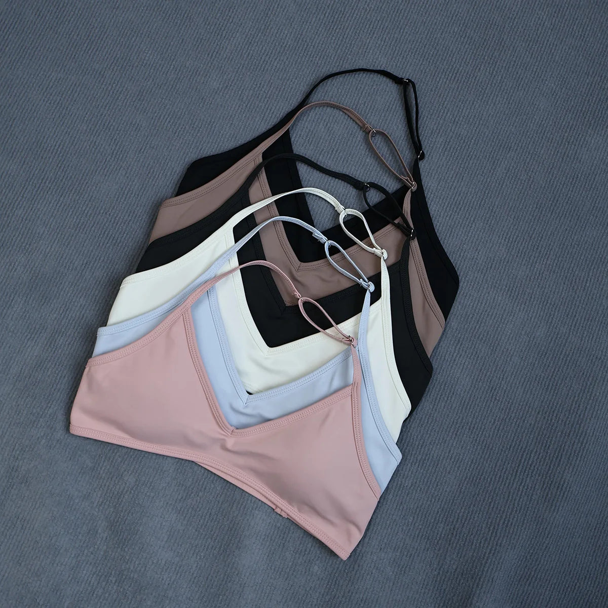 Four wireless sports bra cups in dusty pink, light blue, white, and black, arranged in a fan shape on a textured gray background.