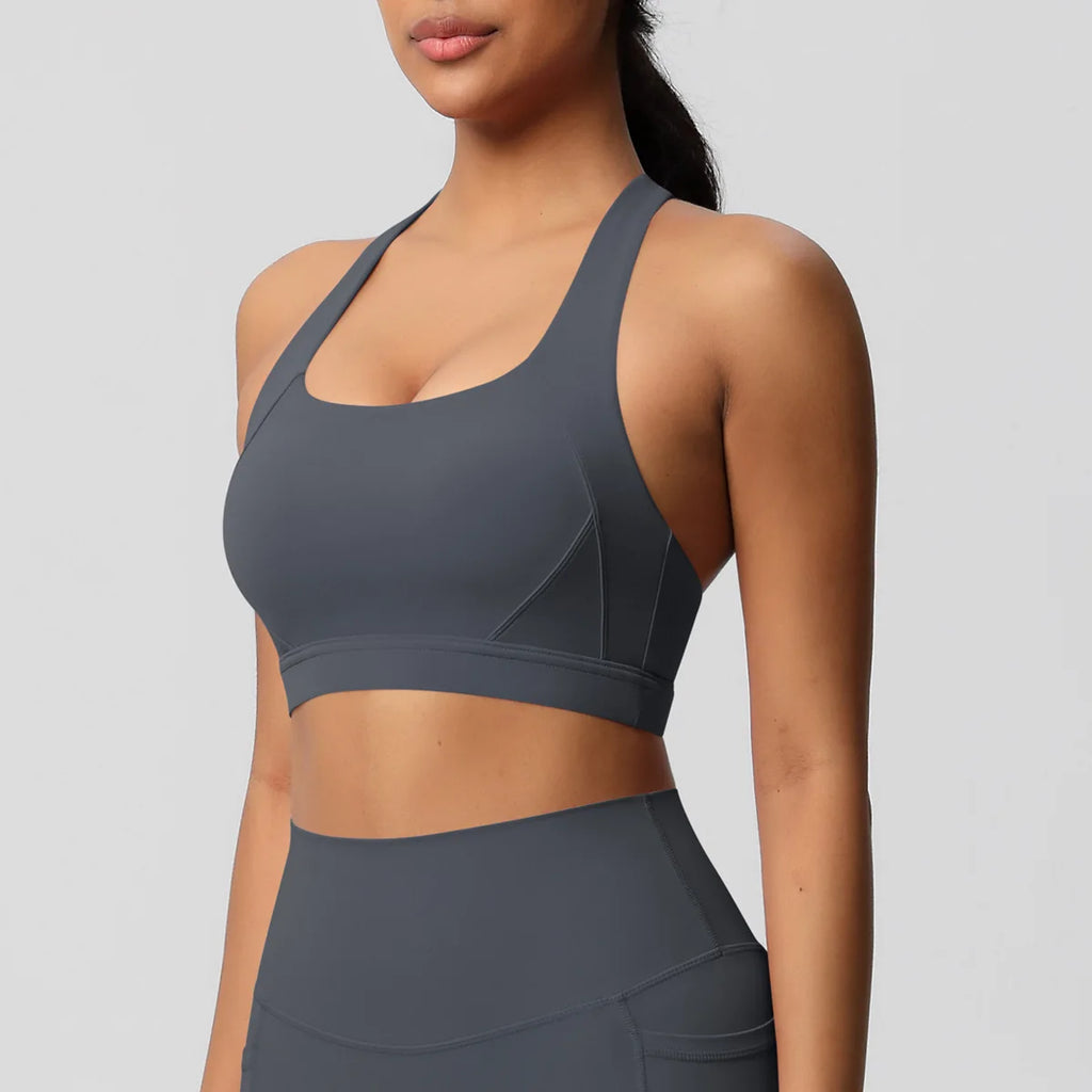 A woman wearing a dark gray athletic sports bra and matching high-waisted leggings against a light gray studio background.