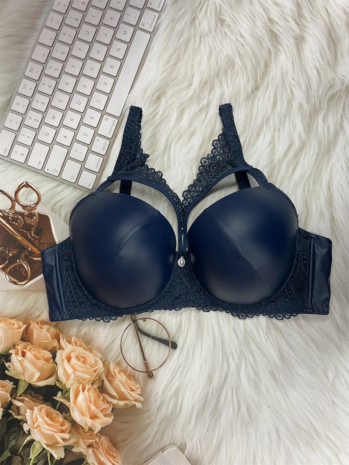 Navy blue bra on a white fur surface with a keyboard, glasses, and flowers in the background.