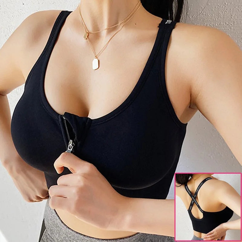 A woman wearing a black sports bra with a front zipper detail, shown from the chest down against a light wall. A small inset in the bottom right shows the back view of the bra with crisscross straps.