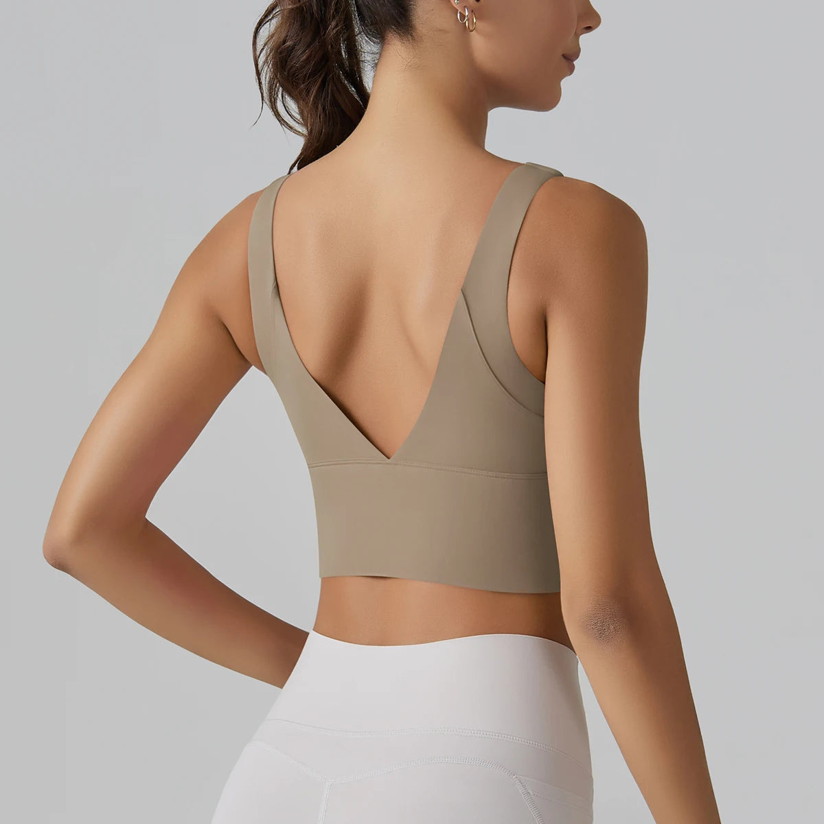 Woman wearing a beige sports bra and white leggings on a gray background