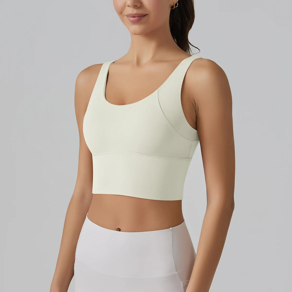 Woman wearing a light green sports bra and white pants on a gray background