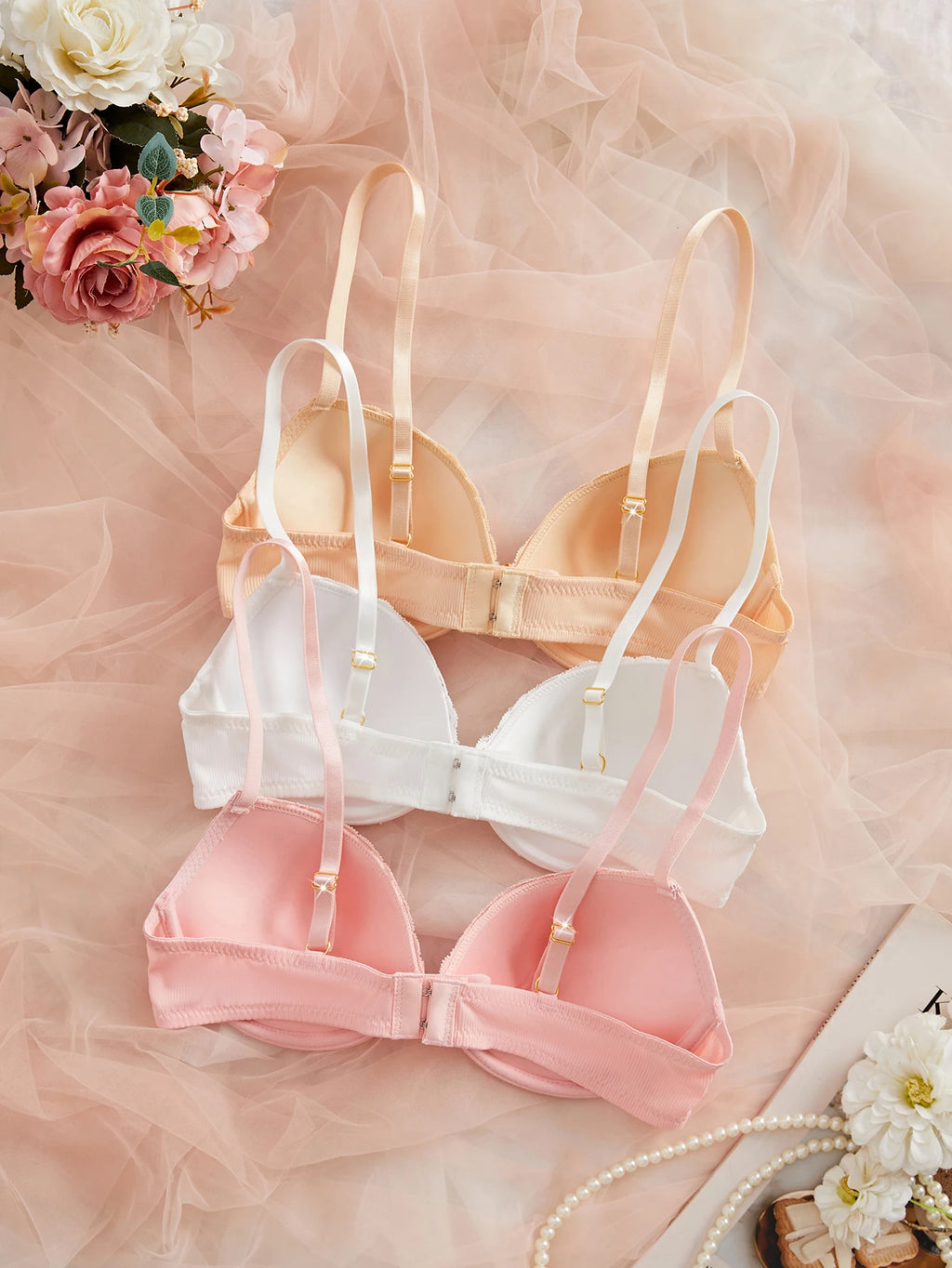 Set of pink and white bras on a soft pink fabric background with flowers.