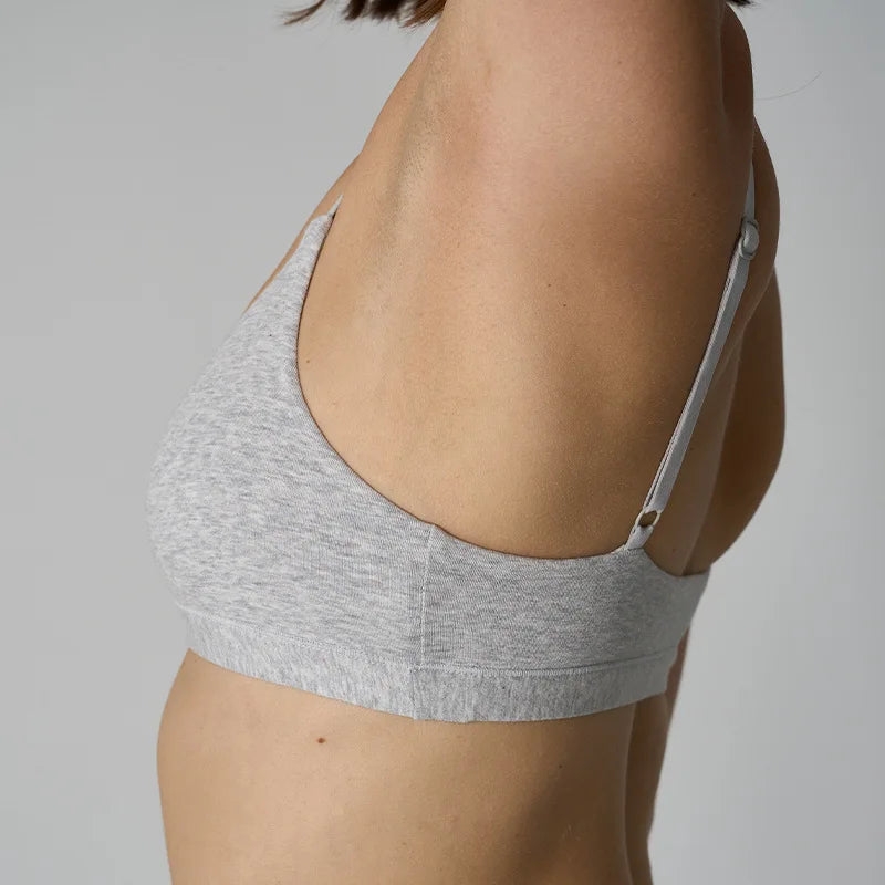 A close-up side view of a woman wearing a light gray heather bralette, showing the back strap and cup design against a plain light gray background.