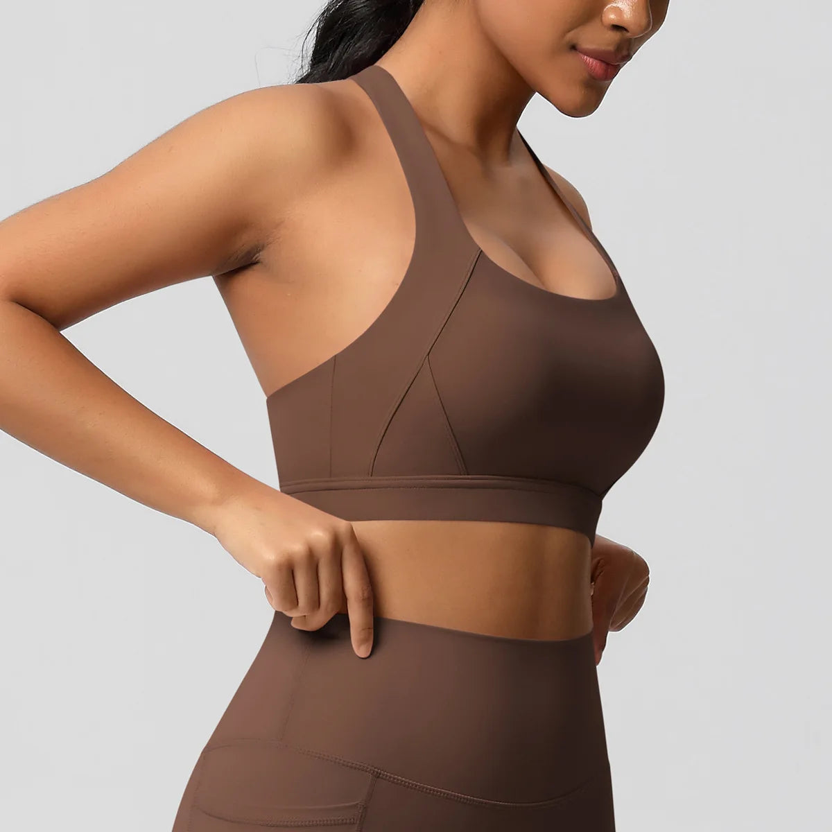 Woman wearing a brown sports bra and leggings on a gray background