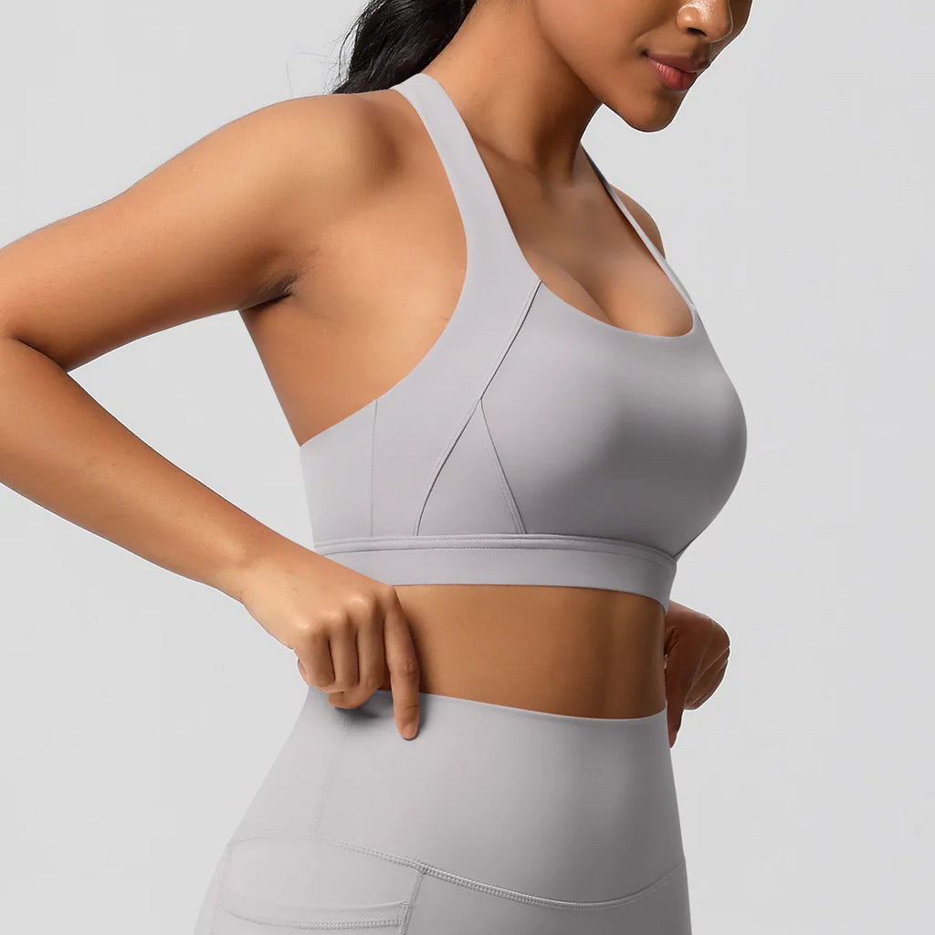 A woman wearing a light gray sports bra and matching high-waisted leggings, shown from the side against a plain light gray background.