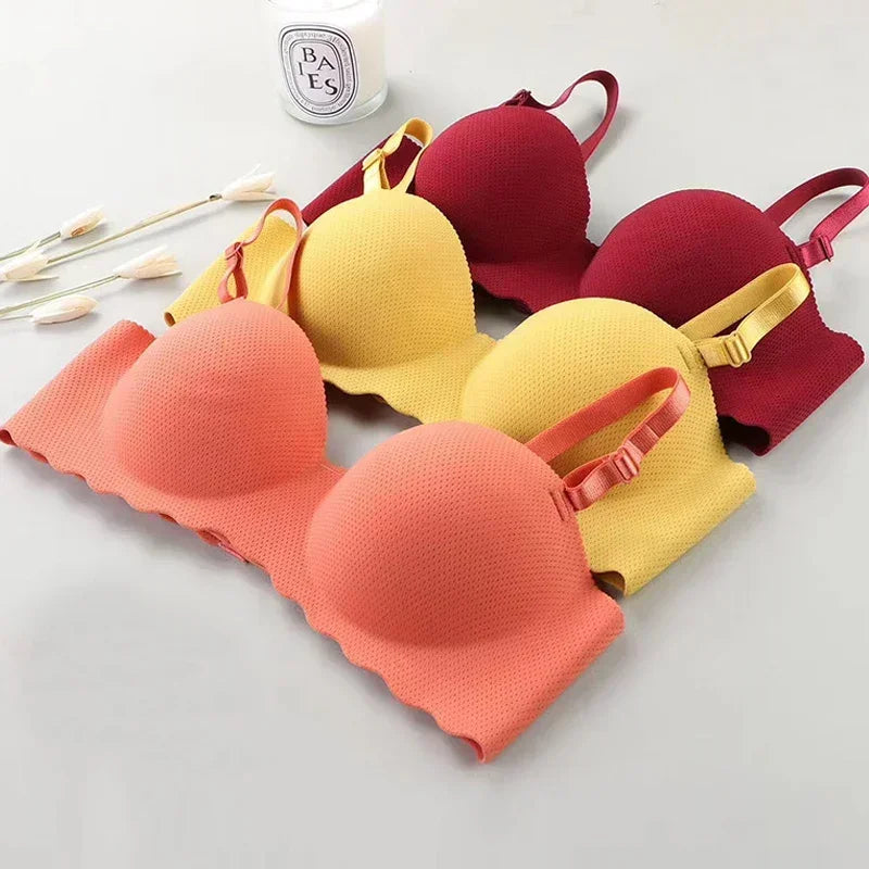 Three colorful bras in red, yellow, and coral on a light gray background with a small bottle of perfume.