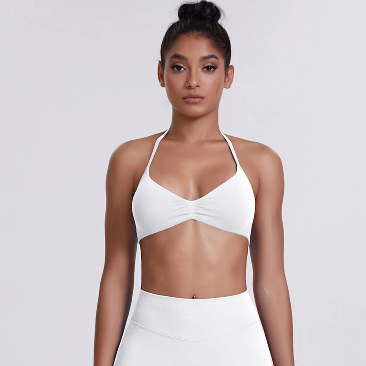 Woman wearing a white sports bra and leggings on a light gray background