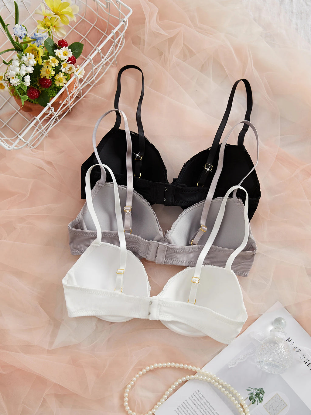 Set of black and white bras on a pink surface with flowers and jewelry in the background