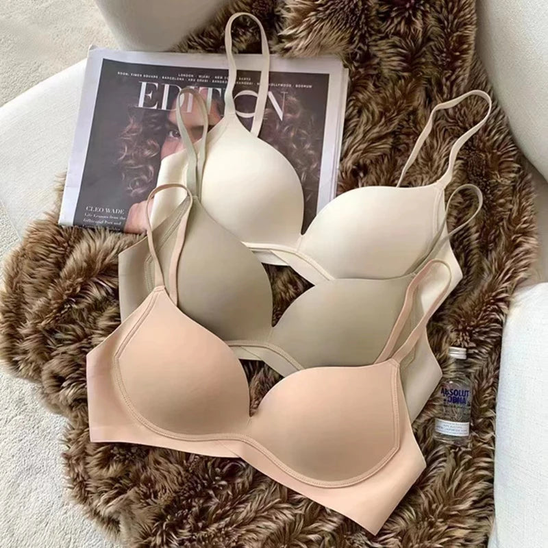 Three wireless underwire bras in soft neutral shades of beige, cream, and light nude, arranged on a brown faux fur blanket with a magazine and a small bottle nearby.