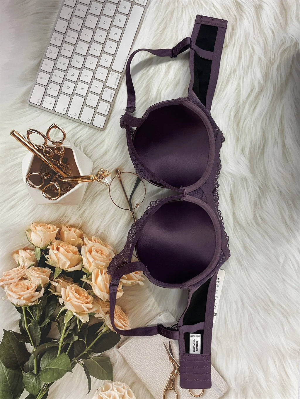 Purple bra on a white surface with flowers, keyboard, and scissors.