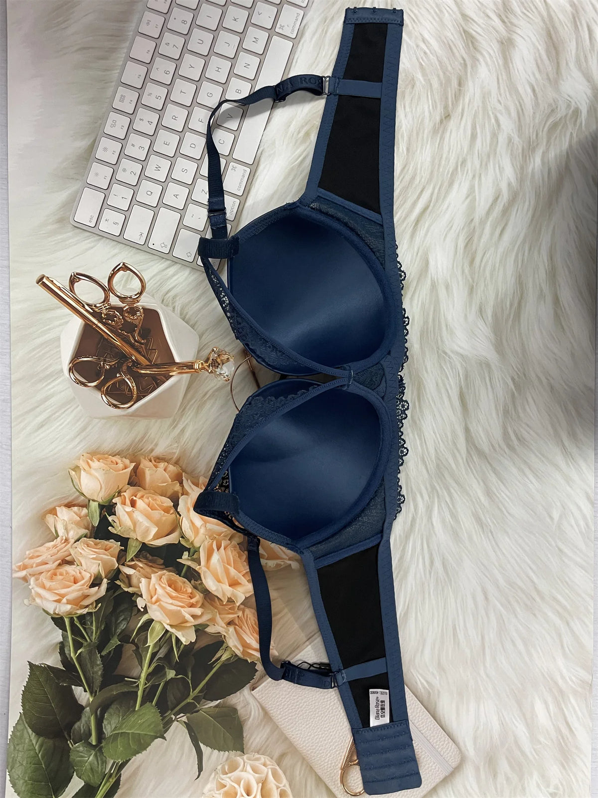 Navy blue bra on a white fur surface with flowers and a keyboard in the background