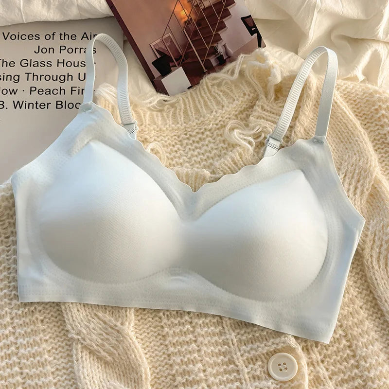 A white wireless bra with scalloped edges and adjustable shoulder straps, laid flat on a cream-colored knit sweater with a magazine in the background.
