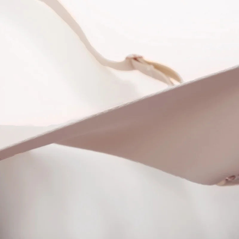 Close-up of a pale blush pink garment, likely a bra or undergarment, showing the smooth fabric and a small metallic hook closure against a white background.