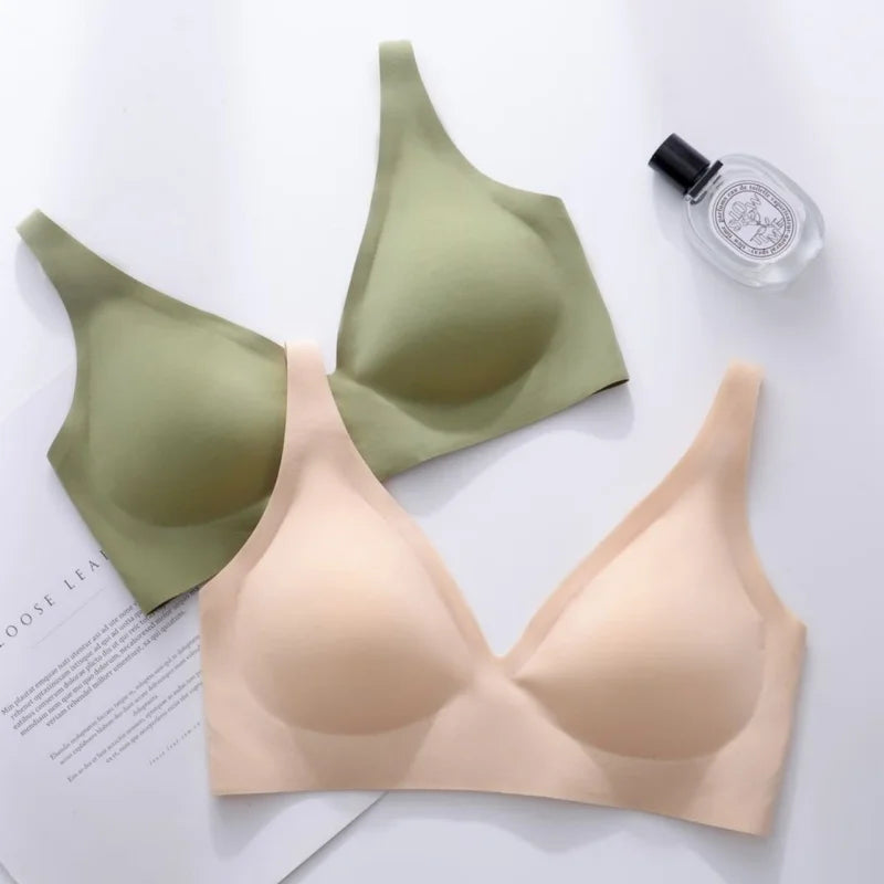 Two bras in green and beige on a white surface with a perfume bottle.