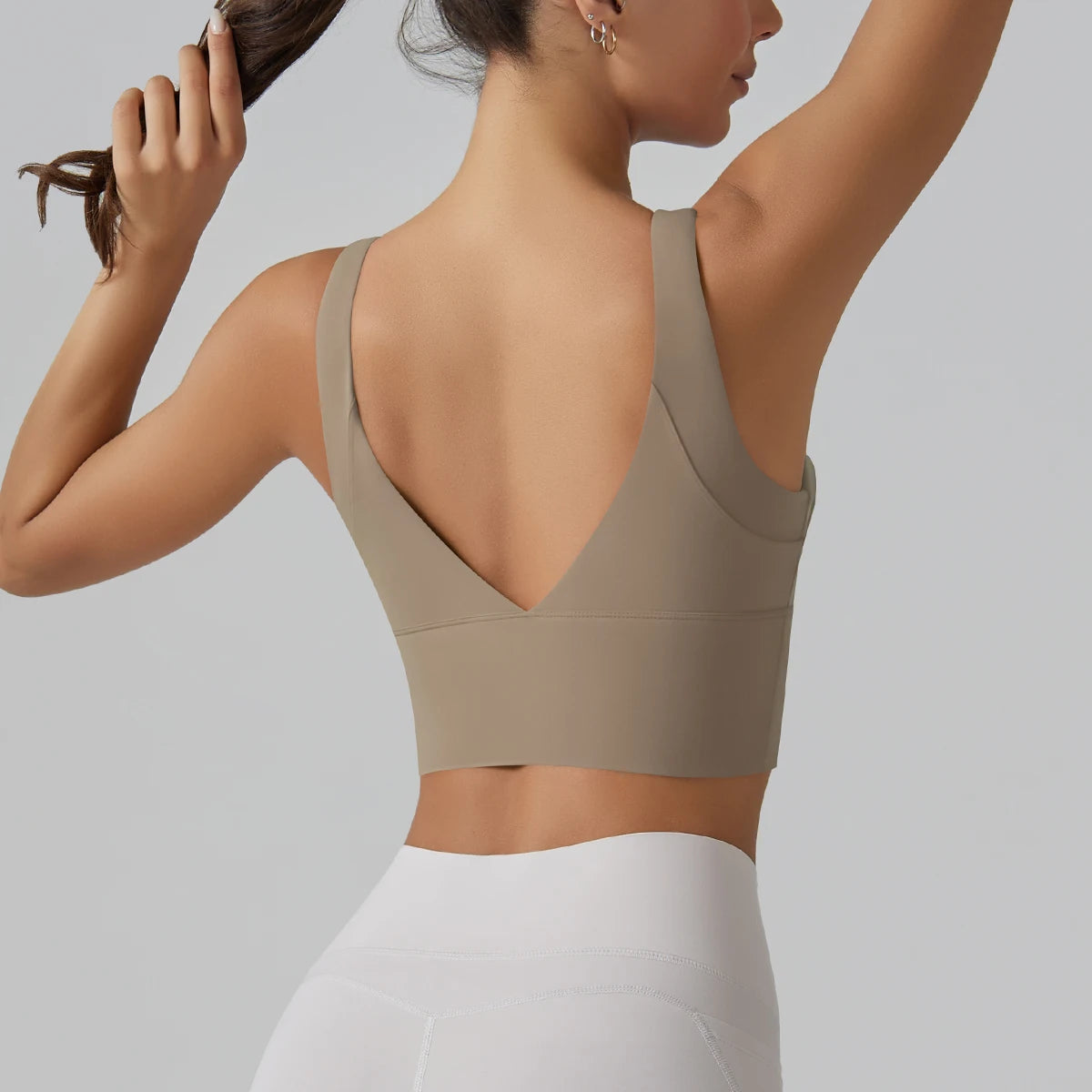 Woman wearing a beige sports bra and white leggings against a gray background