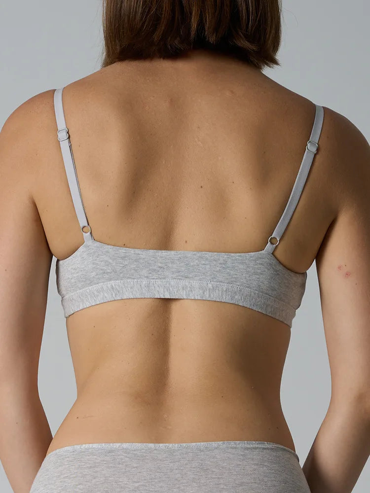 Rear view of a woman wearing a light gray heather bralette with thin adjustable straps and a wide underband, shown against a plain light gray background.