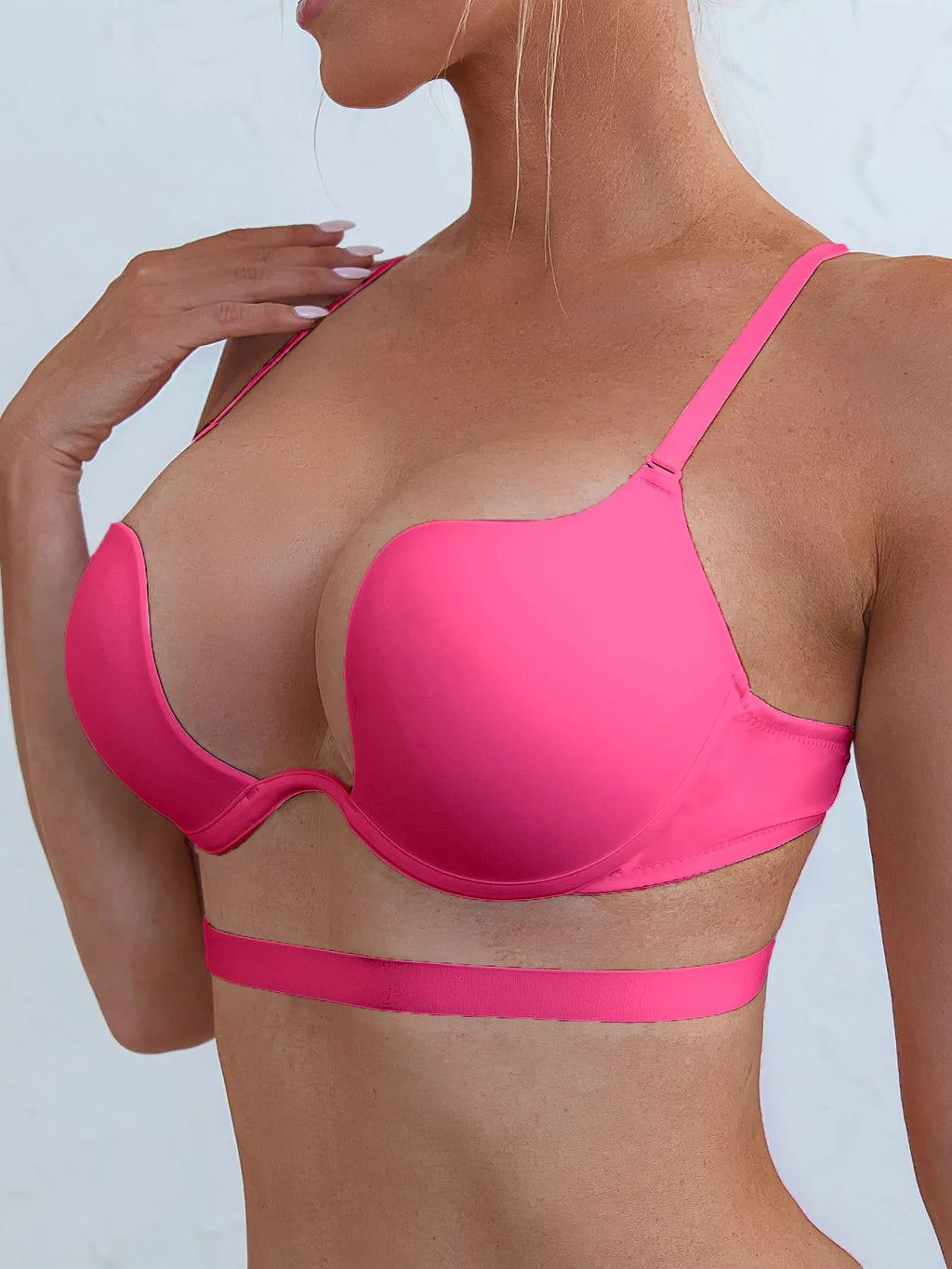 A woman wearing a bright hot pink seamless underwire bra and matching pink waist strap, shown from the side against a light gray background.