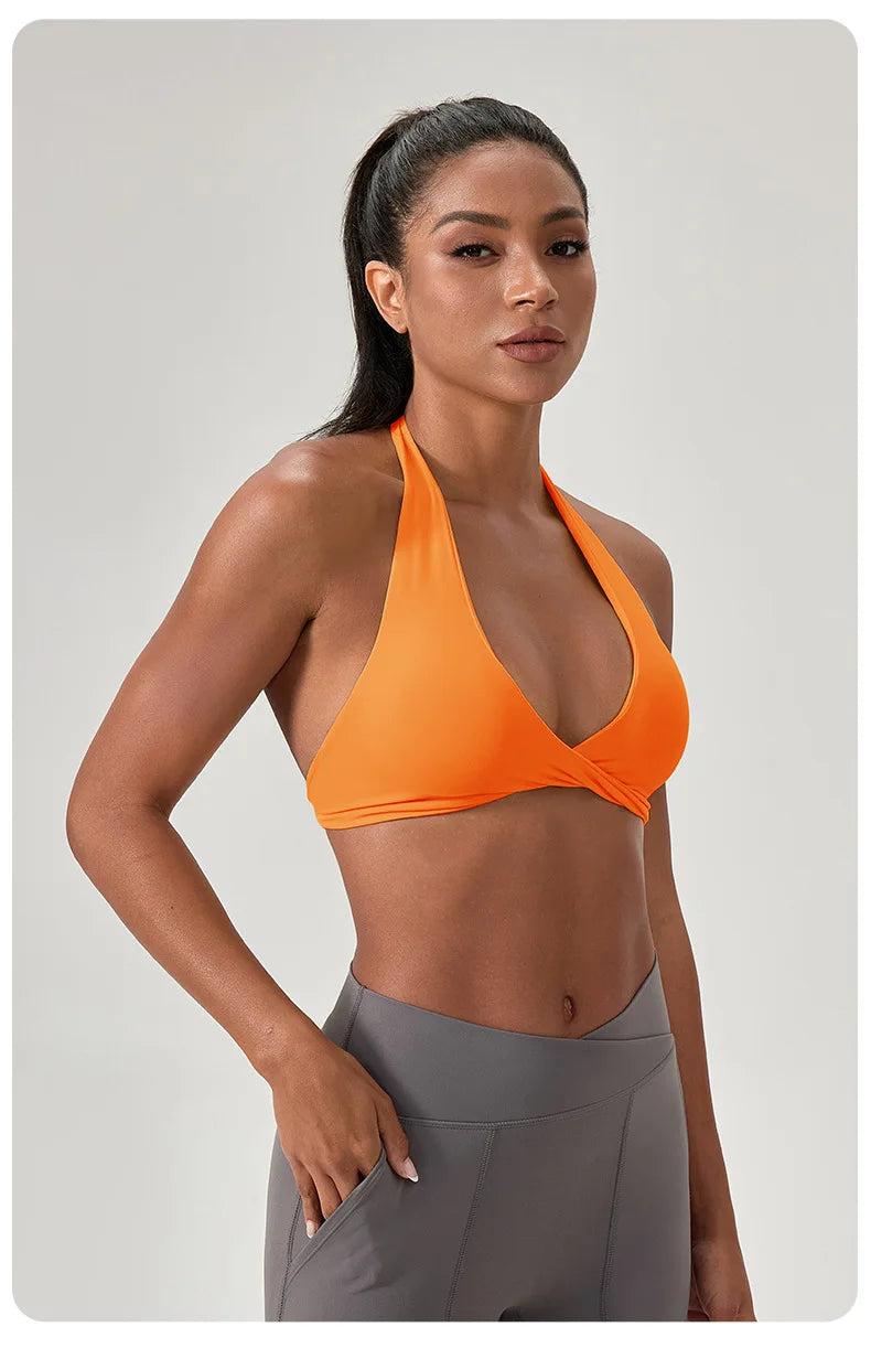 Woman wearing an orange sports bra and gray leggings on a light gray background