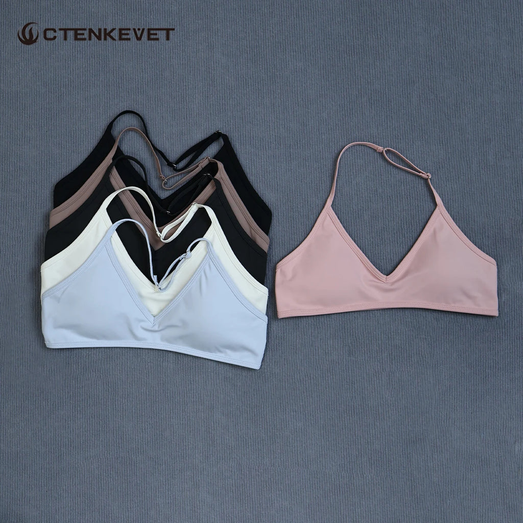Four women's sports bra cups with a V-neckline and double shoulder straps, arranged on a textured gray background. The front-most bra is light blue, layered over black, taupe, and white versions, with a separate light pink bra displayed to the right.