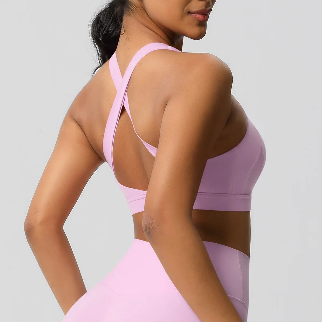 A woman wearing a light pink sports bra and matching high-waisted leggings, shown from the back against a light gray studio background.