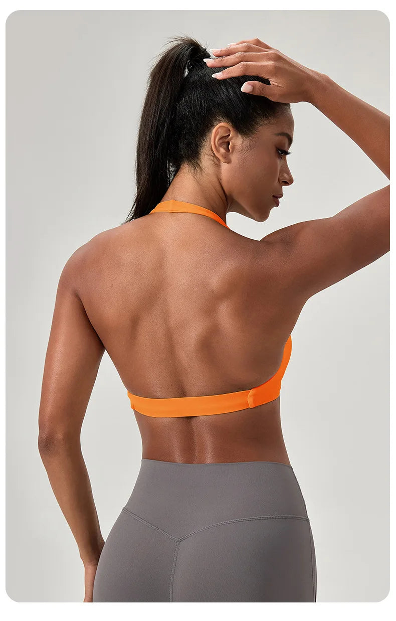 Woman wearing an orange sports bra and gray leggings against a neutral background