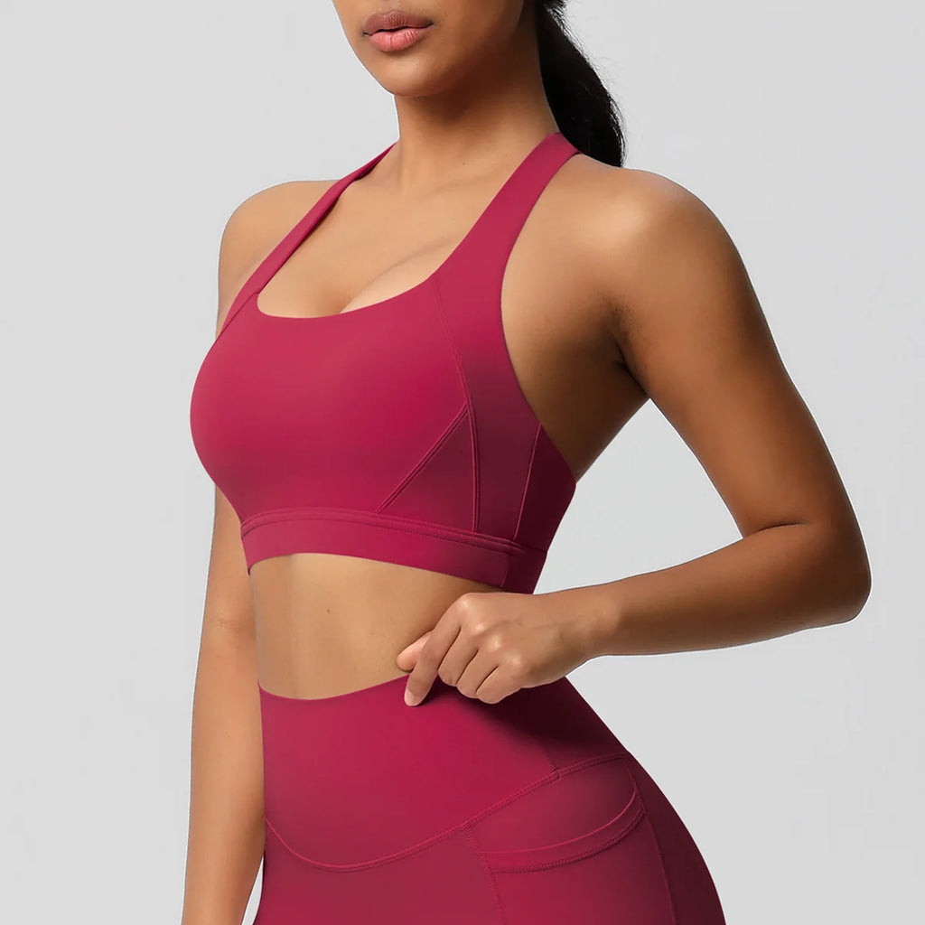 A woman wearing a matching athletic set in a deep magenta pink, featuring a scoop-neck sports bra and high-waisted leggings, shown against a solid light gray background.