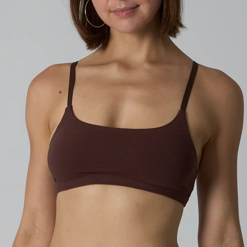 A woman wearing a dark brown scoop-neck bralette with thin straps, shown from the chest up against a light gray studio background.