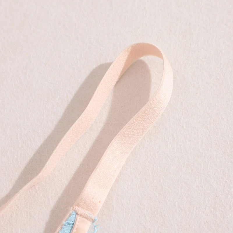 A close-up of a light peach-pink fabric strap, likely from a bra or garment, laid diagonally on a textured off-white background.