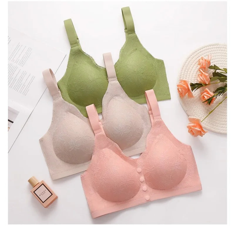 Three bras in green, beige, and pink on a white surface with a small round table and flowers in the background.