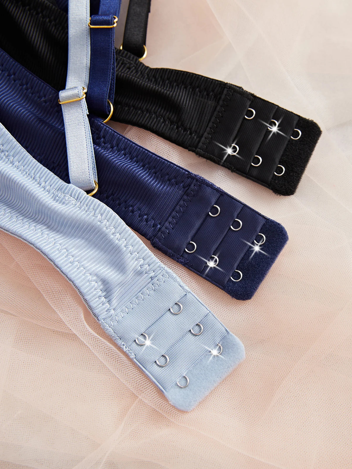 Three pairs of garter straps in black, navy, and light blue on a soft pink background.