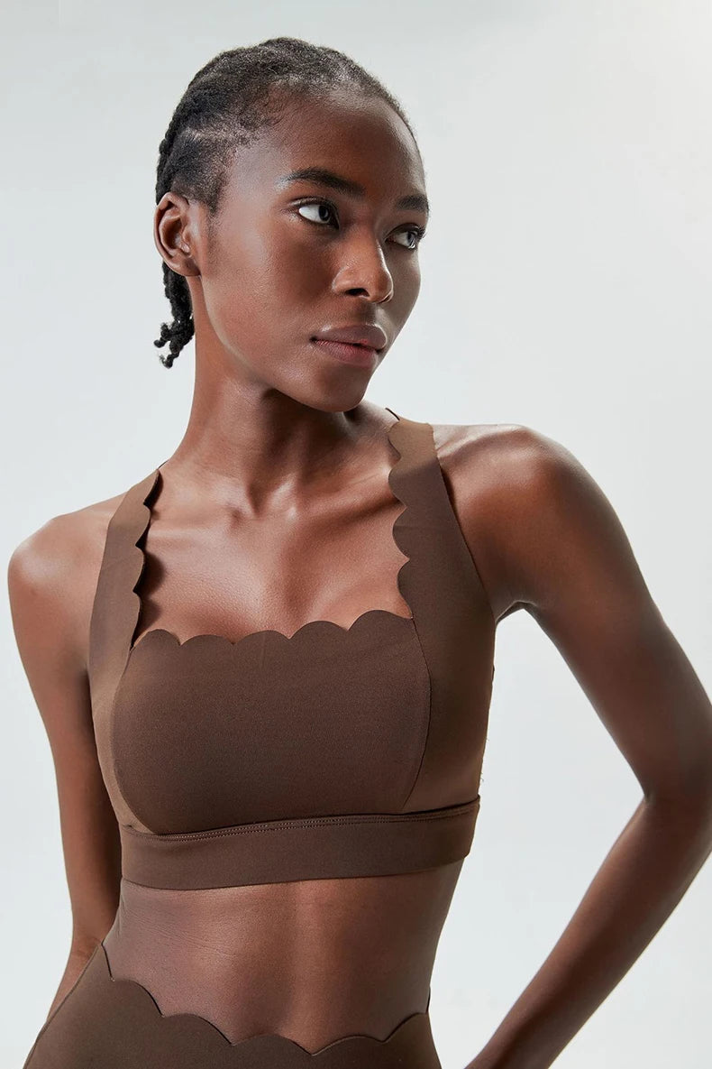 Woman wearing a brown scalloped-edge top against a plain background