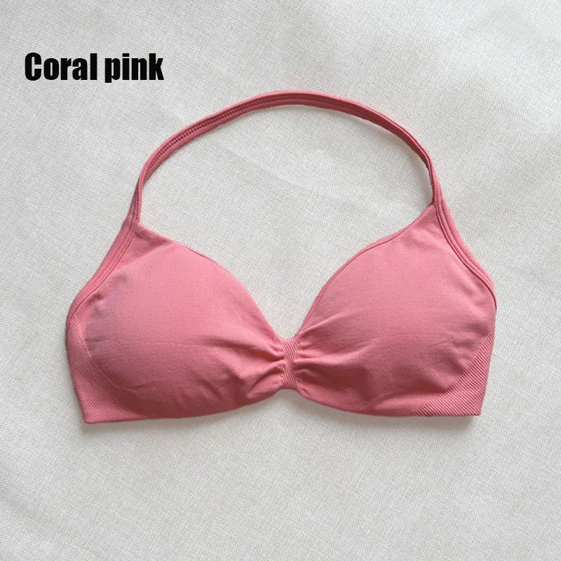 A coral pink bikini top with a halter-style neck and gathered center, laid flat on a light textured fabric background with the text 'Coral pink' in the top-left corner.