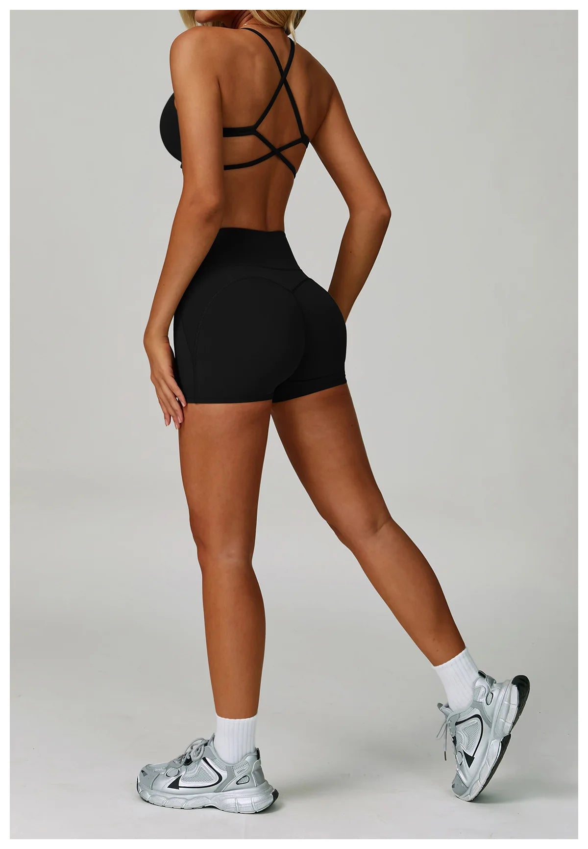 Person wearing a black sports bra and shorts with white sneakers on a light gray background