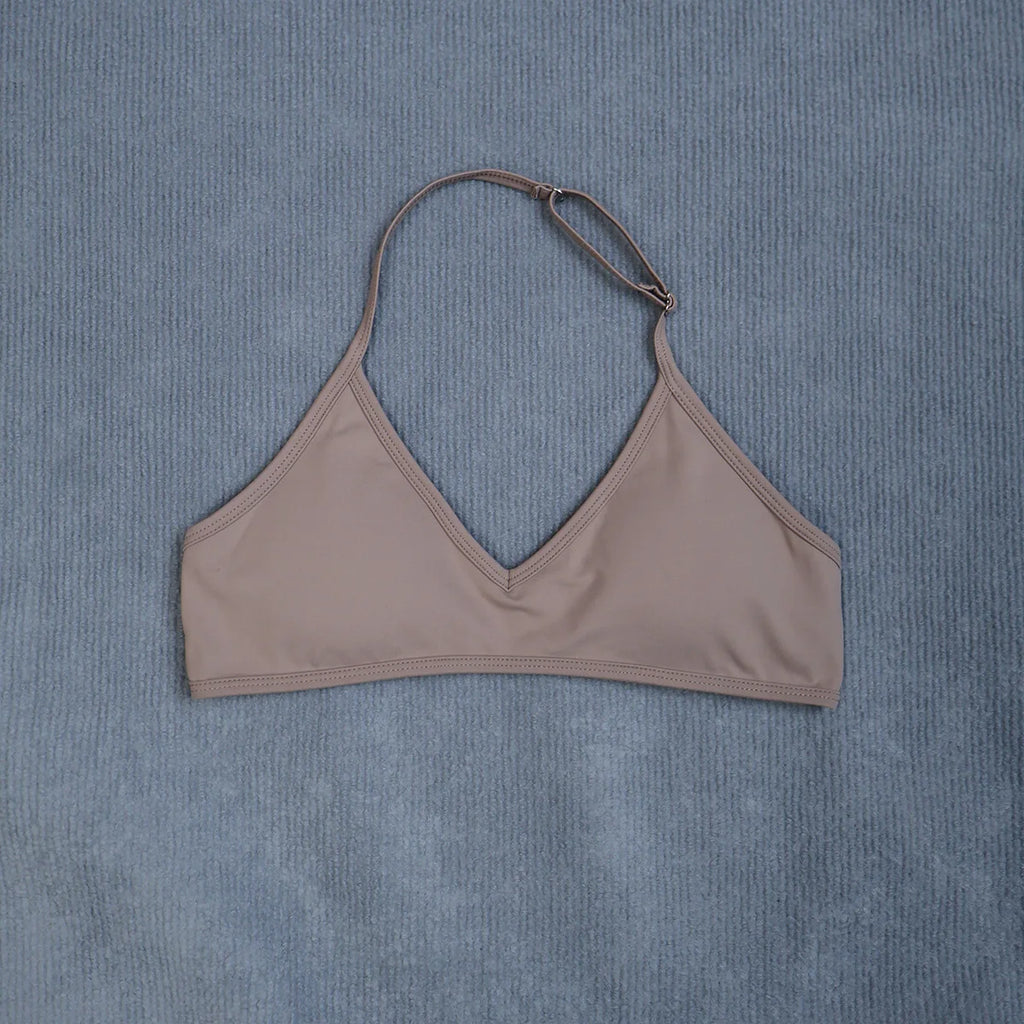 A taupe halter bikini top laid flat on a textured blue-gray fabric background.