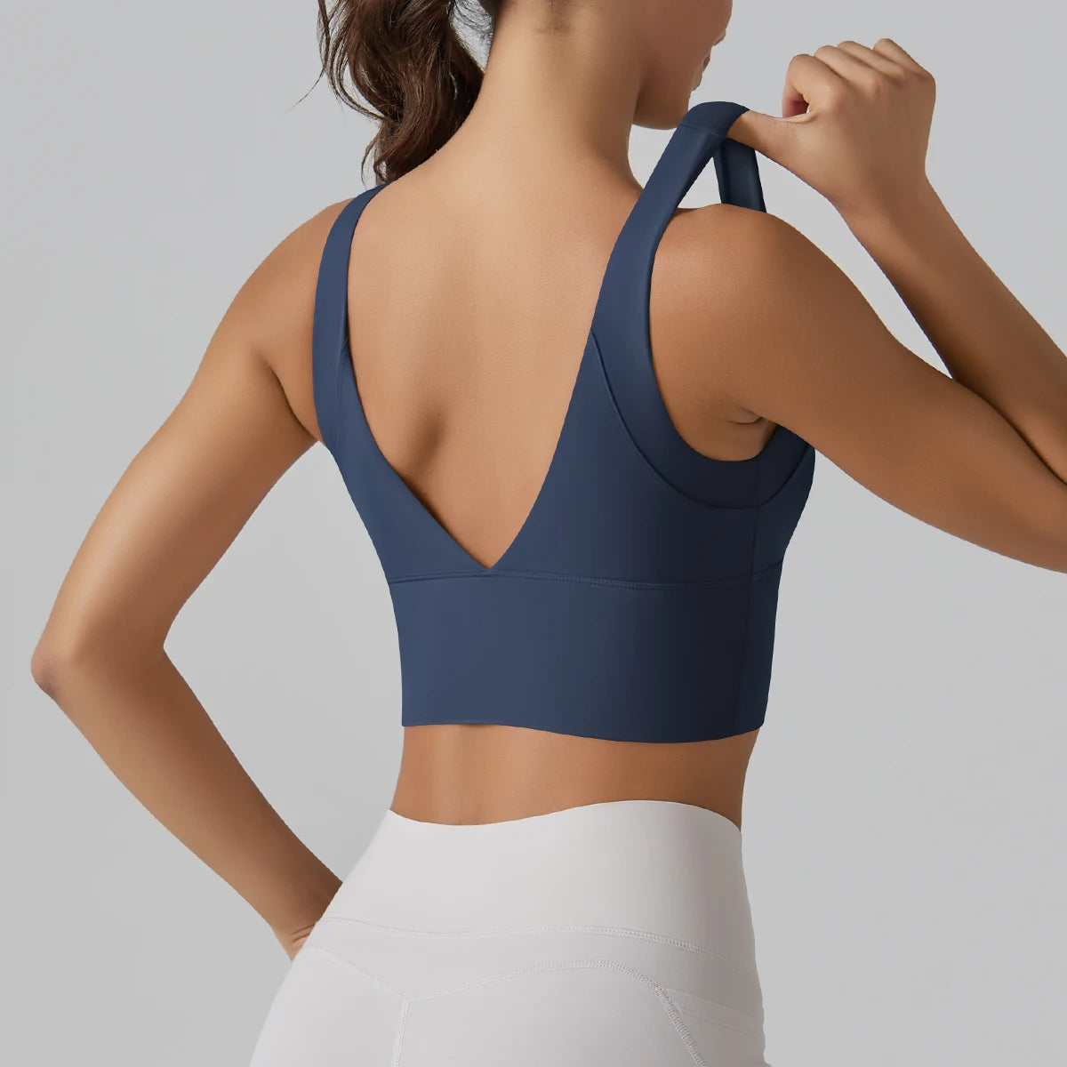 Person wearing a navy blue sports bra and white pants on a gray background