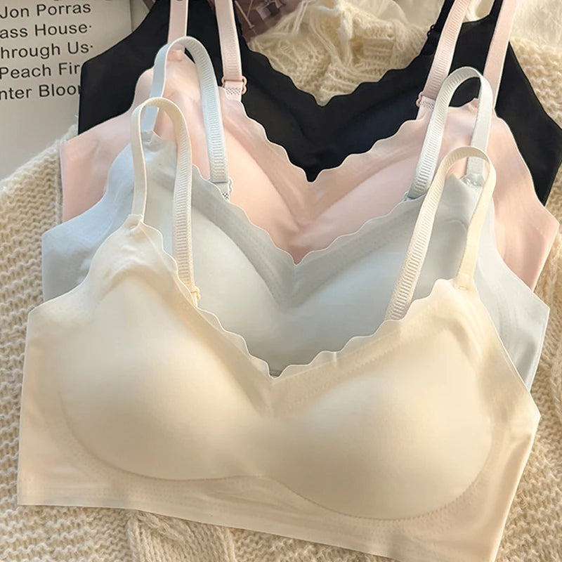 Three wireless underwire bras with scalloped edges in cream, light blue, and pale pink, layered together on a textured knit surface.