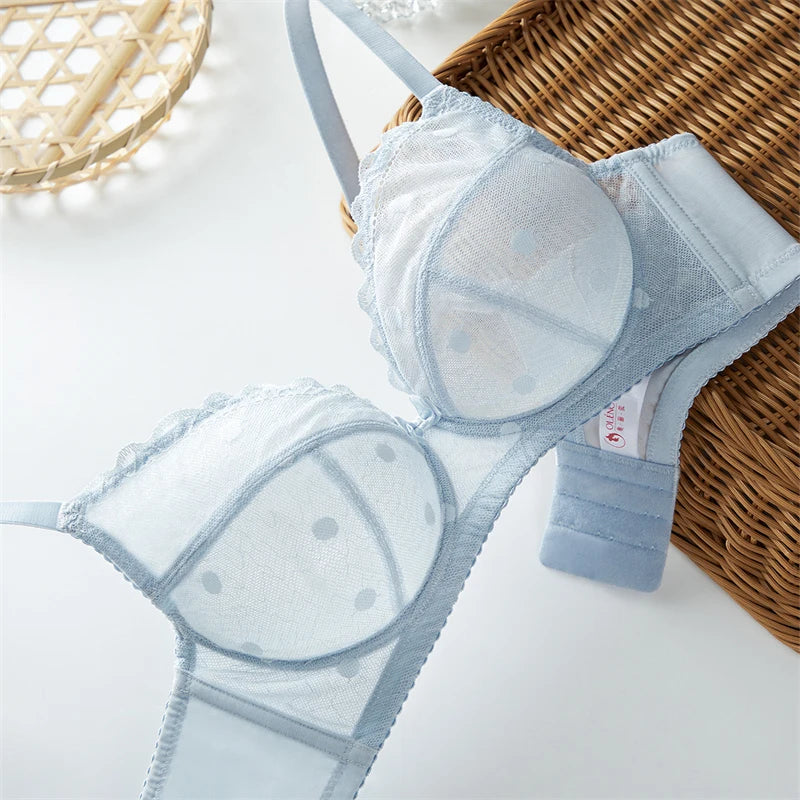 A light blue sheer mesh bralette with white polka dots and lace trim, styled on a white surface next to a brown wicker basket.