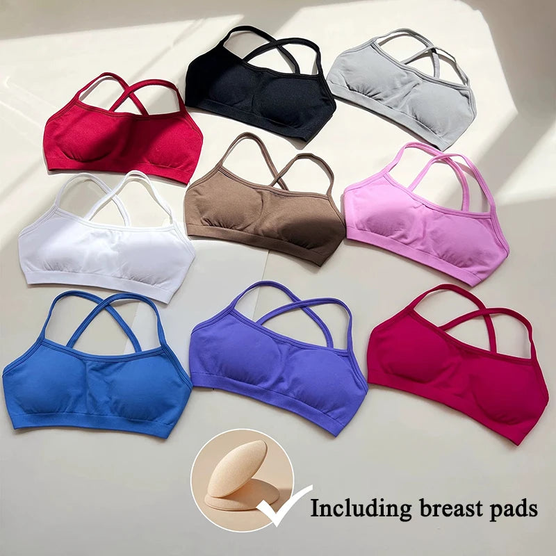 Nine wireless sports bra-style underwired cups in assorted colors are arranged on a light surface with diagonal shadows. The set includes red, black, gray, white, brown, pink, blue, purple, and magenta, and a circular inset at the bottom shows beige breast pads with the text 'Including breast pads'.