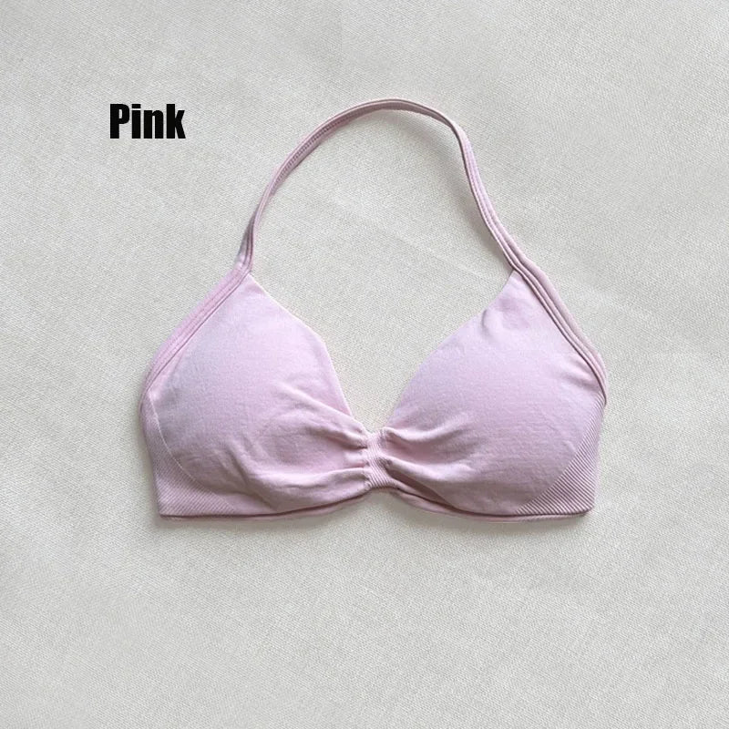A light pink halter bikini top with a gathered front detail, laid flat on a textured off-white fabric background with the word 'Pink' printed in the upper left.