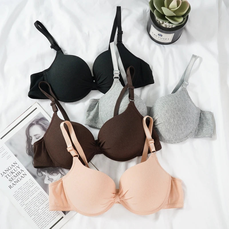 Four bras in black, brown, gray, and beige on a white surface with a plant and magazine.