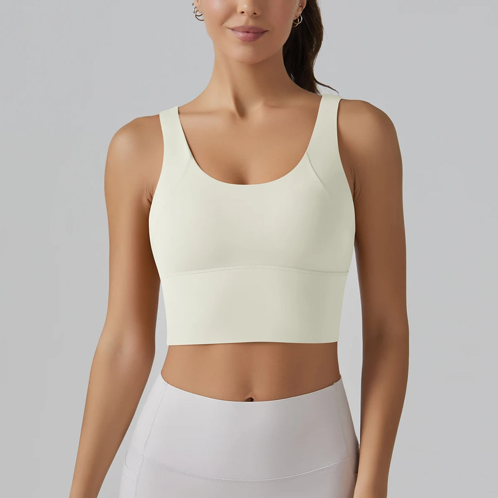 Woman wearing a light-colored sports bra and leggings on a plain background