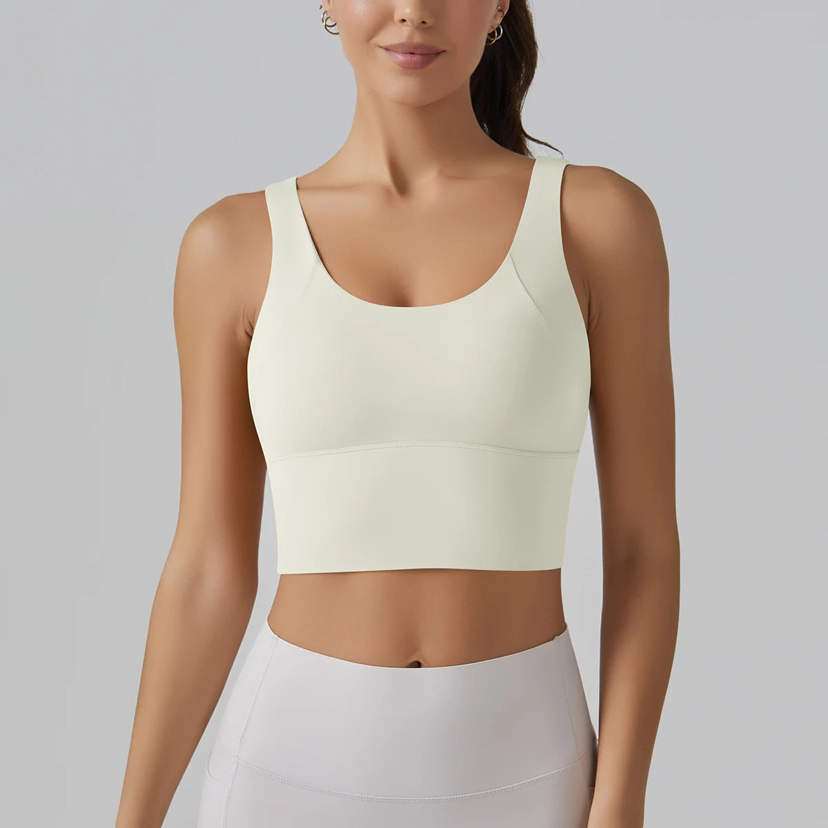 Woman wearing a light-colored sports bra and leggings on a plain background