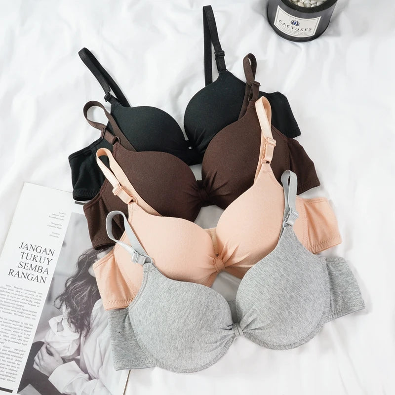 Four bras in black, brown, beige, and gray on a white surface with a magazine and bottle.
